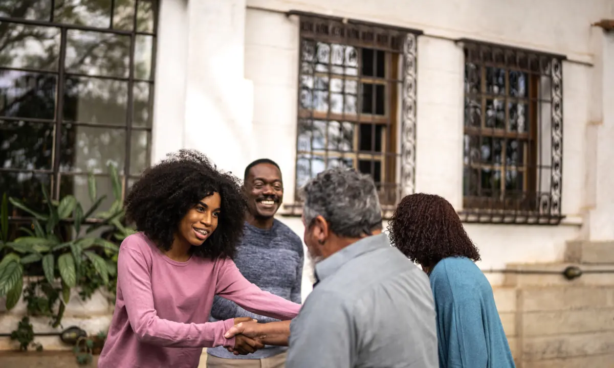 Neighbors shaking hands and smiling in front of a home