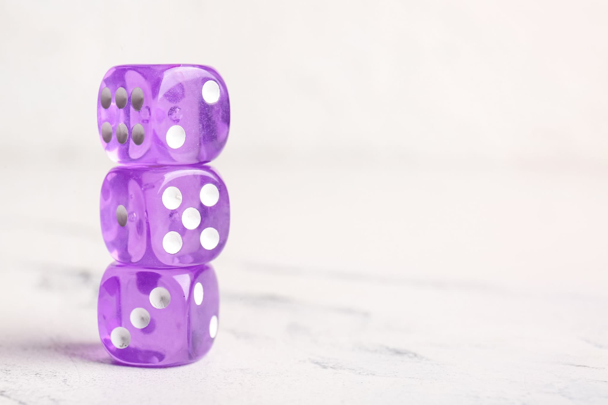 Three translucent purple dice stacked on a light surface.