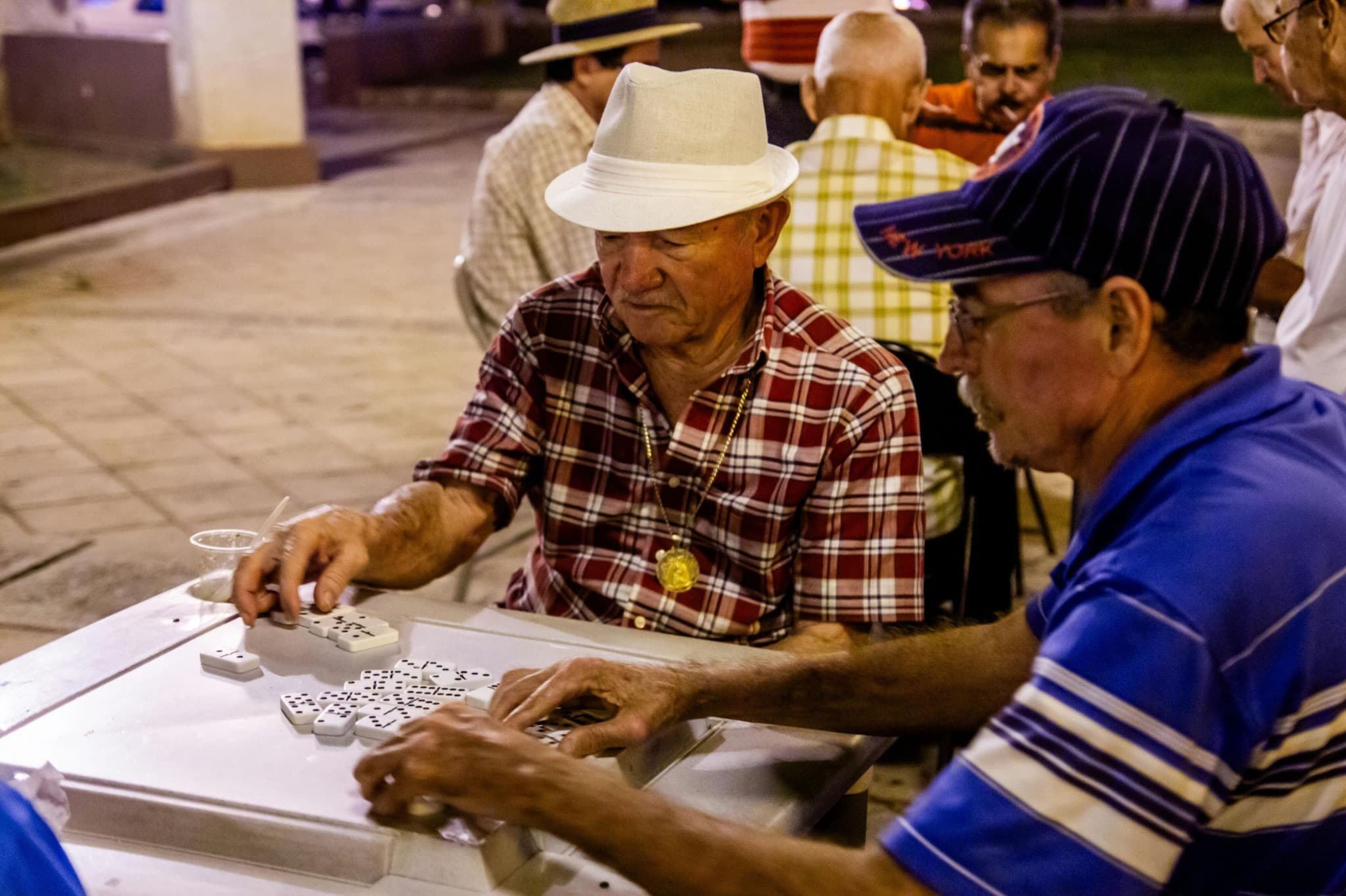 Players mixing white domino tiles on an outdoor table.
