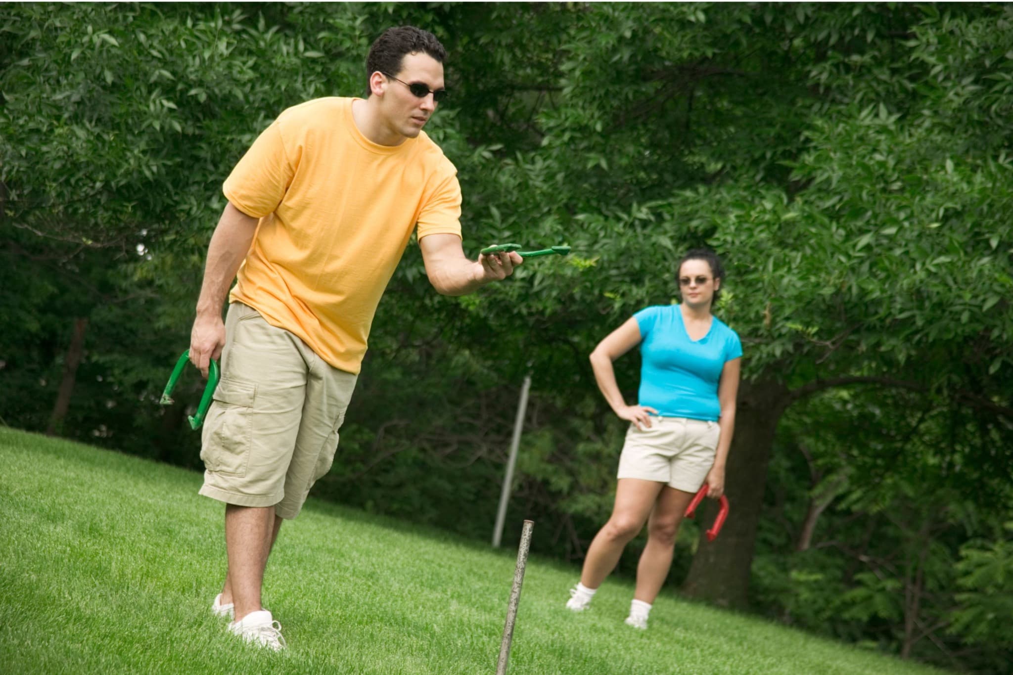 A player preparing to pitch a green horseshoe while another player watches on the lawn.
