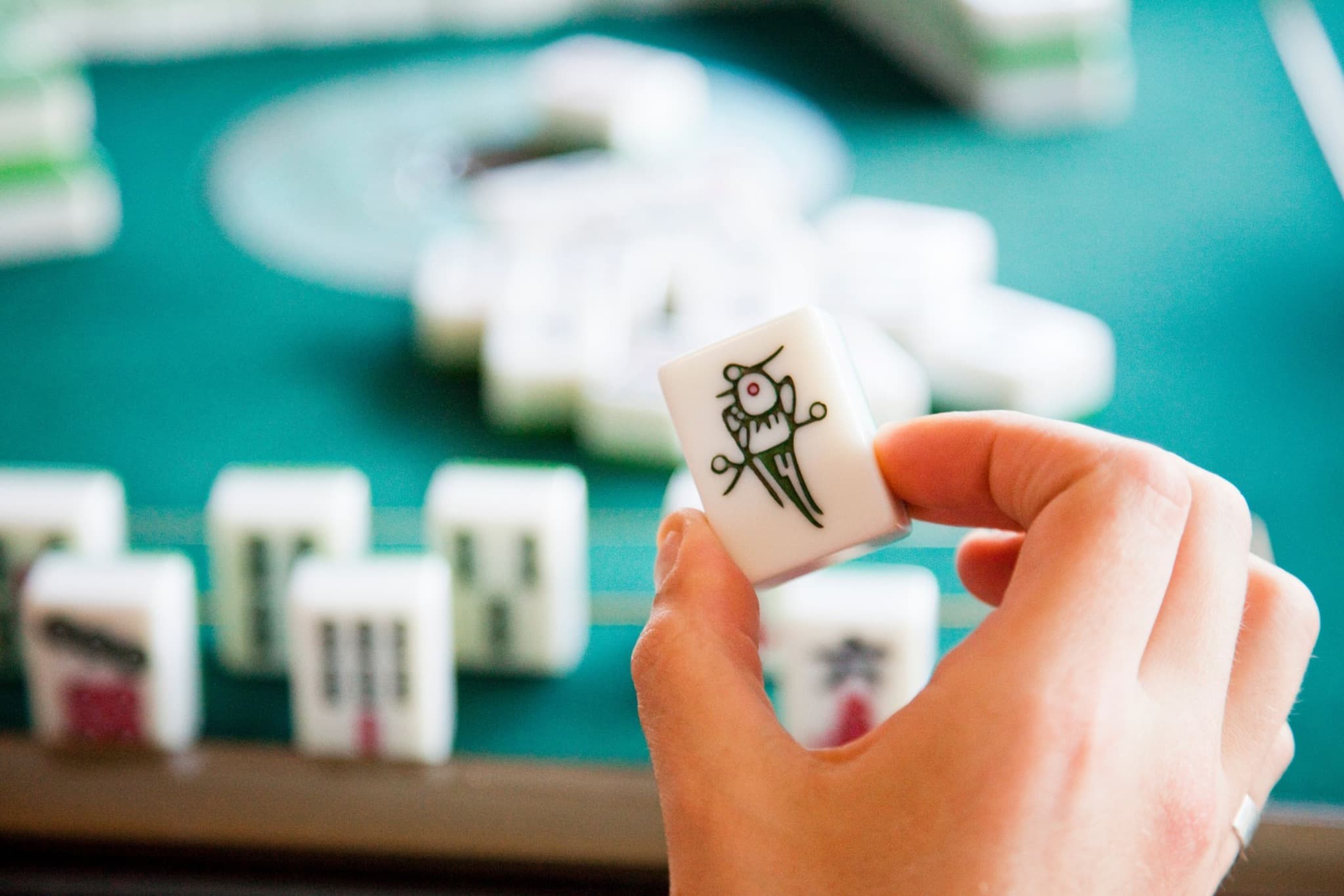 A hand holding a bird-design mahjong tile above a green playing surface.
