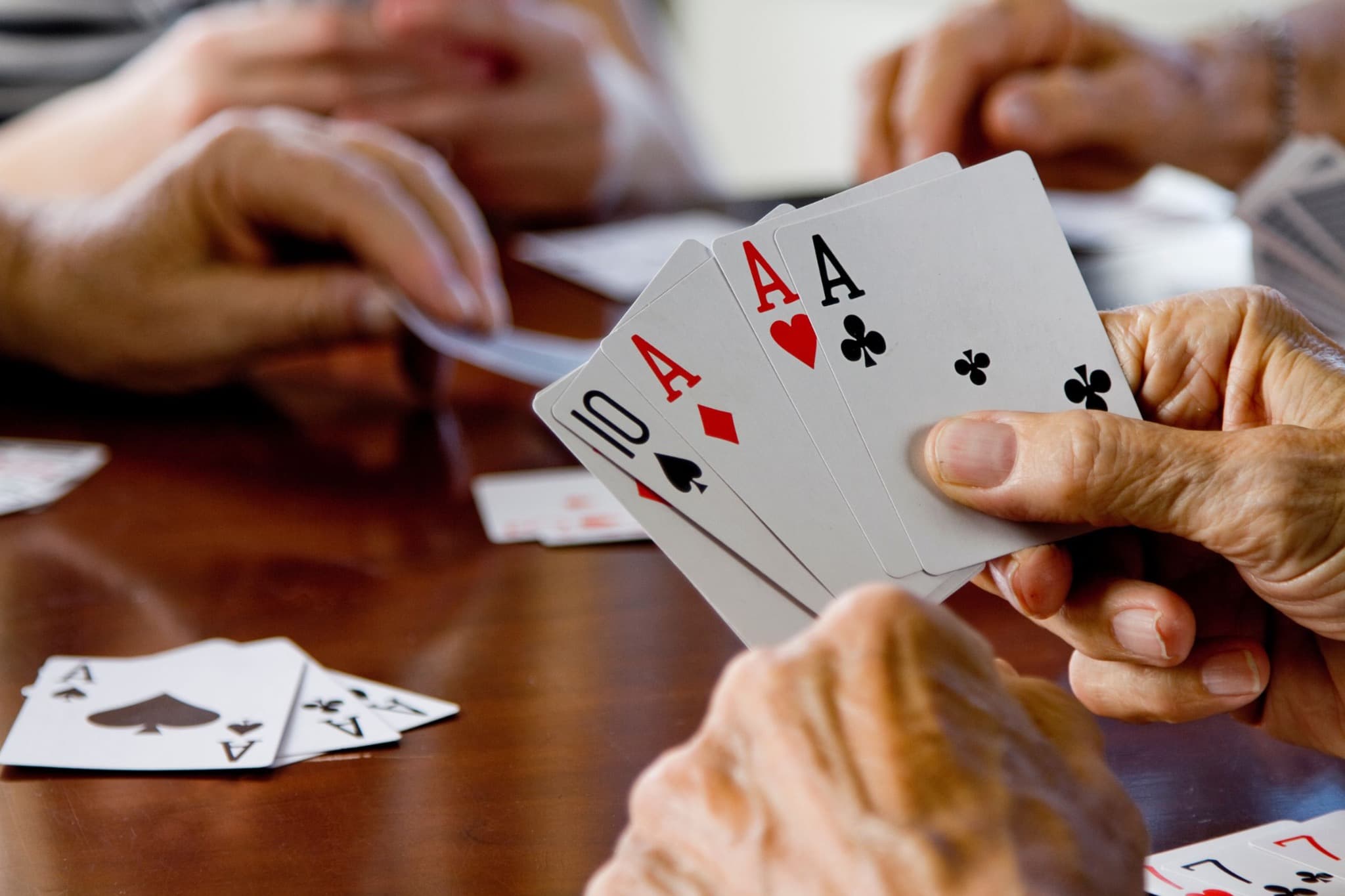 A player holding three aces and a ten while others play cards around the table.
