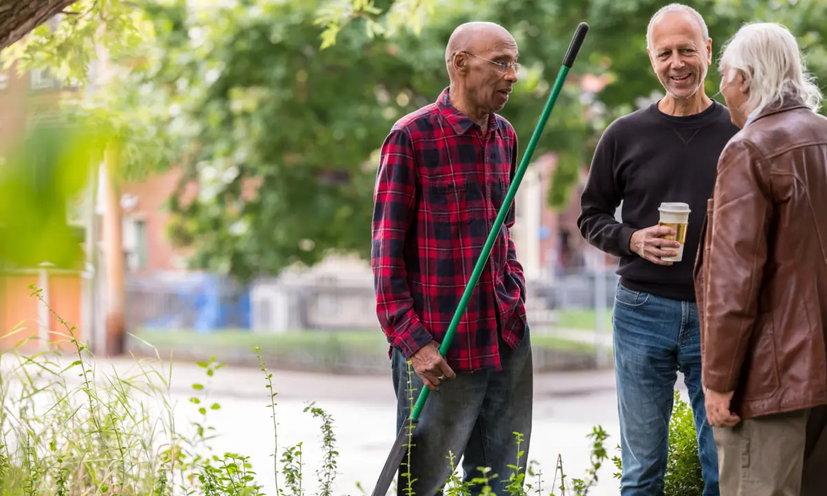 Three neighbors chatting outdoors with a garden tool