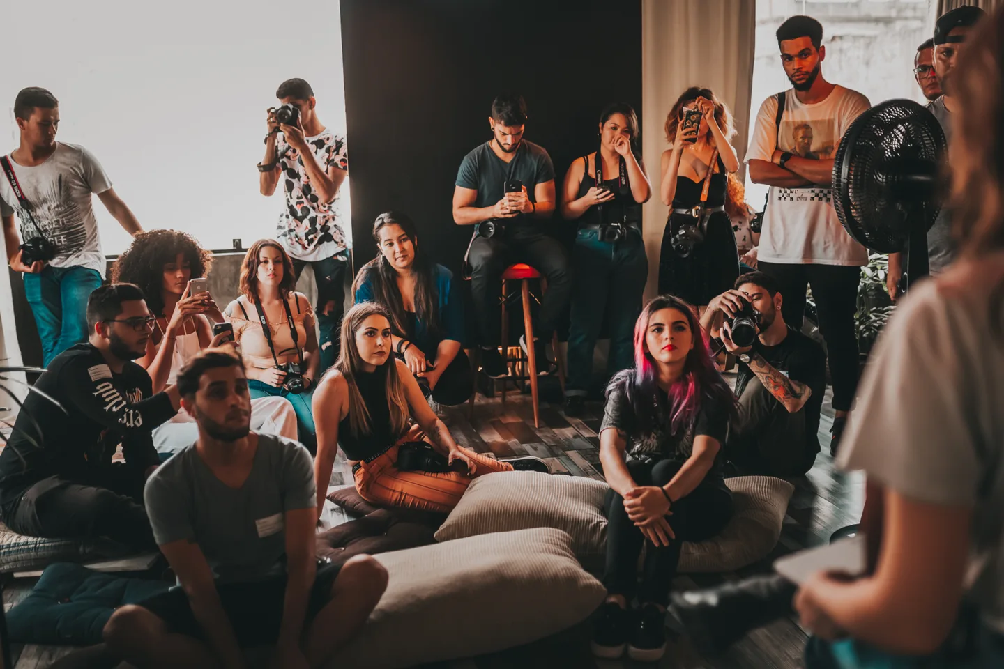 A group with cameras listening to a speaker during an indoor gathering.